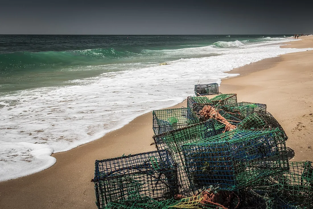Gestapelde groene octopuskorven op het strand van Praia do Barril met branding op de achtergrond