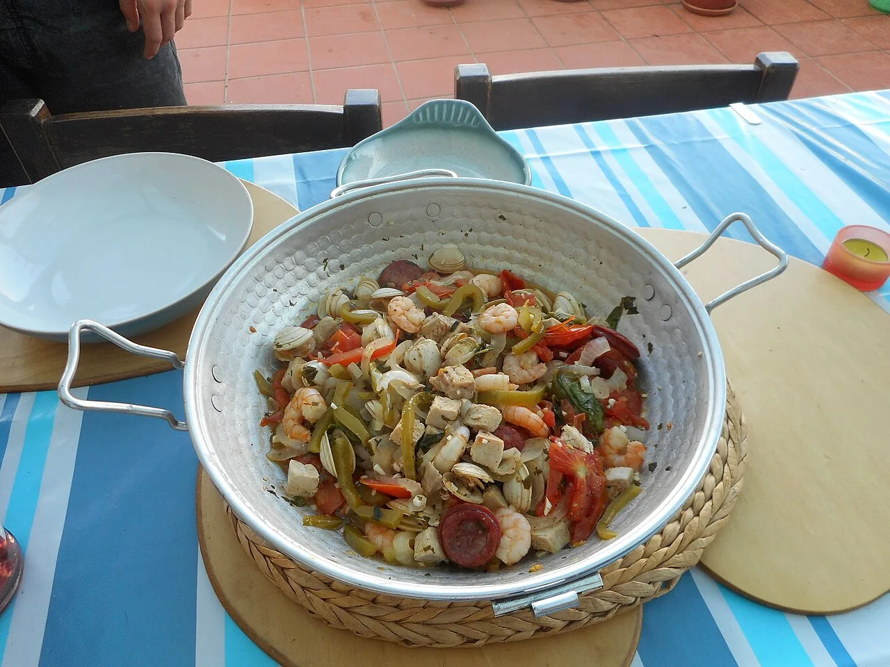 Een geopende koperen cataplana-pan met vis, schaaldieren, paprika en chorizo