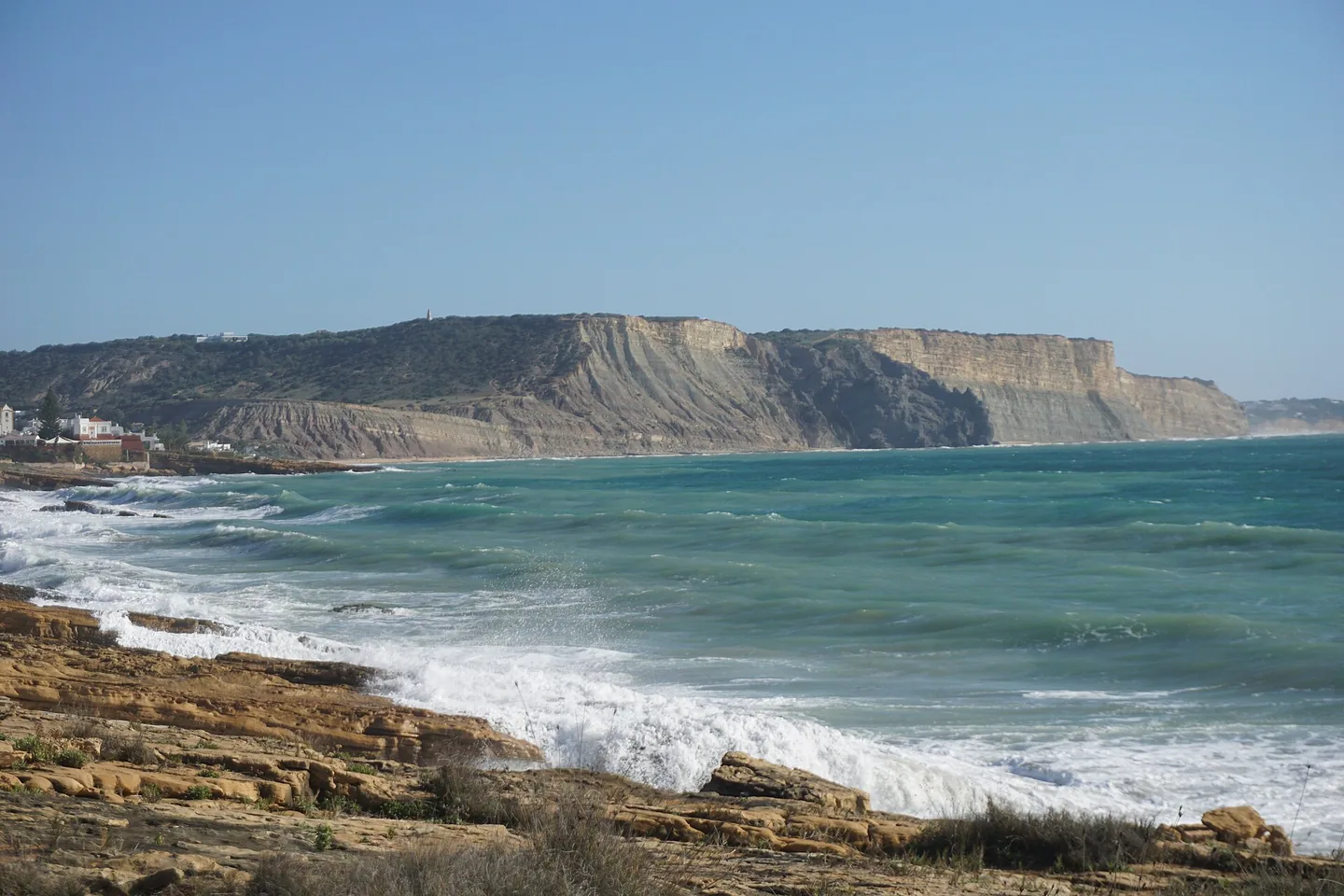 De donkere, vlak afgetopte Rocha Negra boven de branding aan de oostkant van Praia da Luz