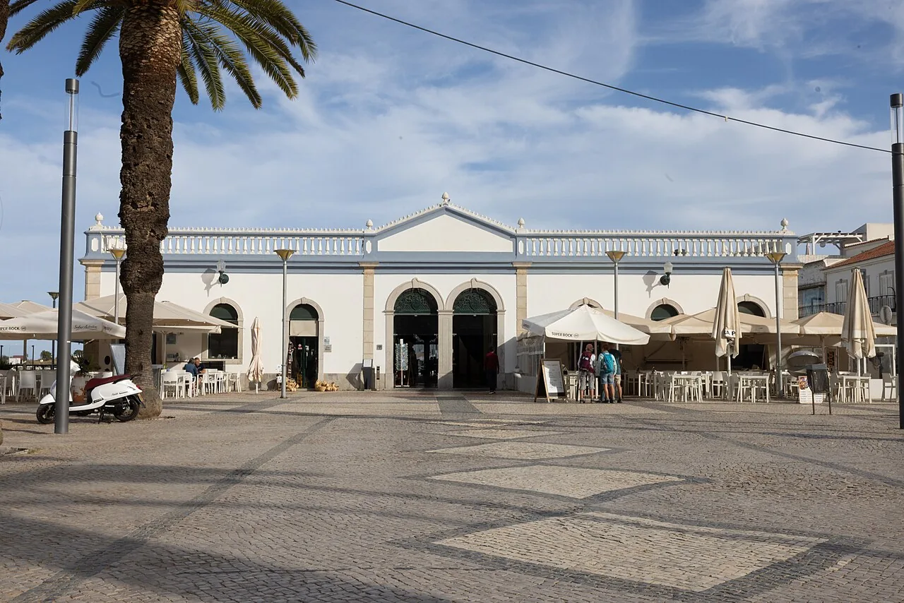 De witte gevel van de Mercado da Ribeira in Tavira met terrassen en parasols op het plein ervoor