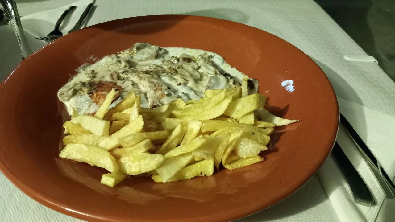 Een aardewerken bord met vlees in een romige champignonsaus en huisgesneden friet