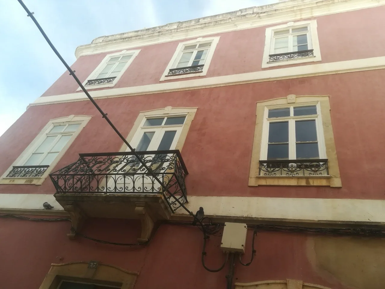 Een oudroze gepleisterde gevel in Olhão met witte kozijnen en een smeedijzeren balkon