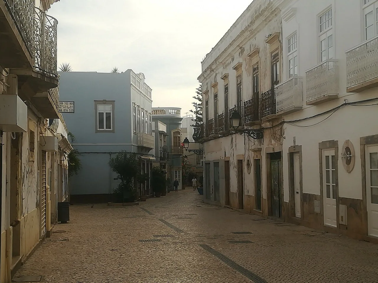 Een lege straat in Olhão in de late namiddag, met kasseien en smeedijzeren balkons aan beide kanten