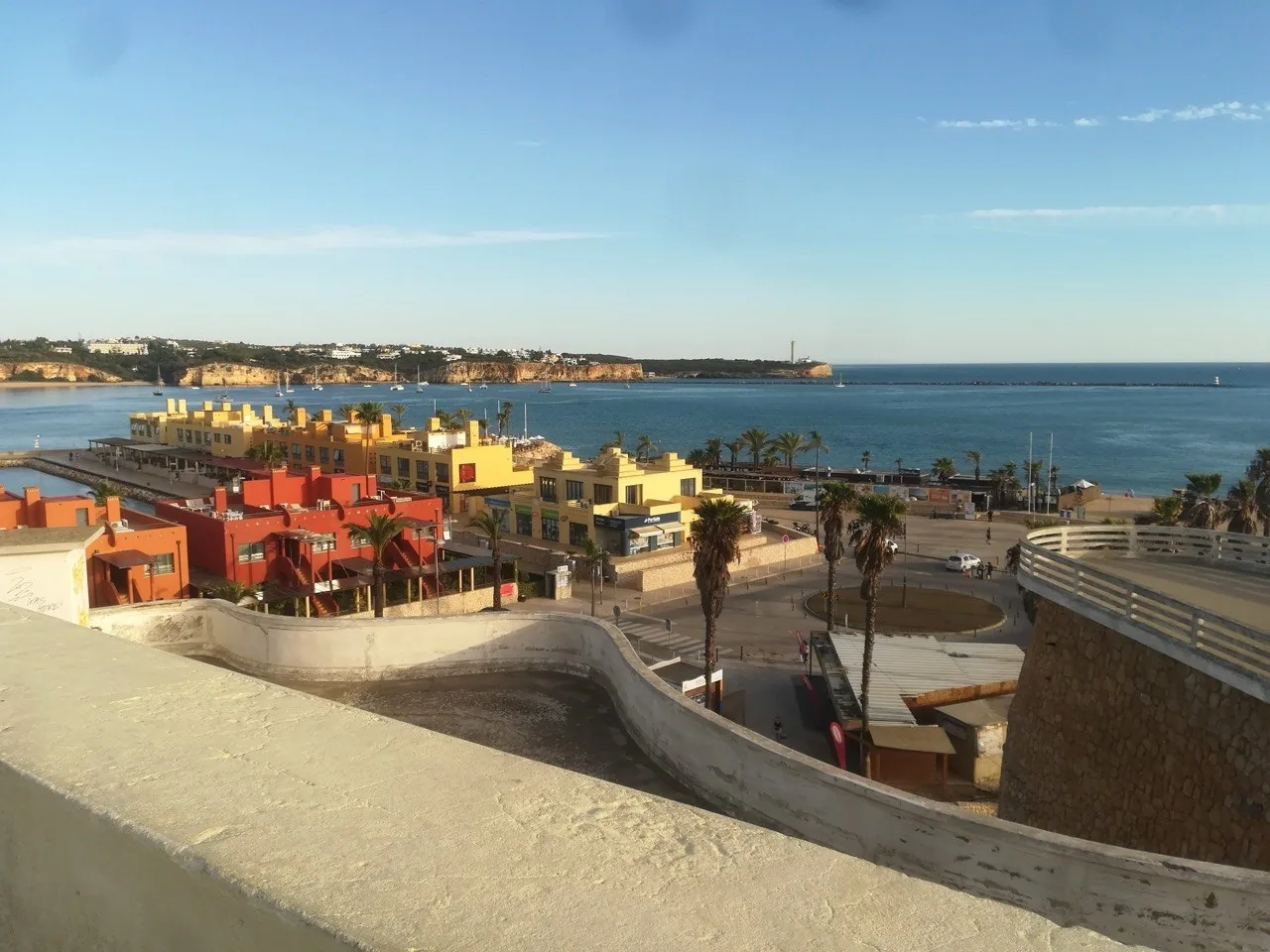 Uitzicht vanaf de muur van het fort van Portimão over de roodgedekte gebouwen aan de haven, met palmen en de kust erachter