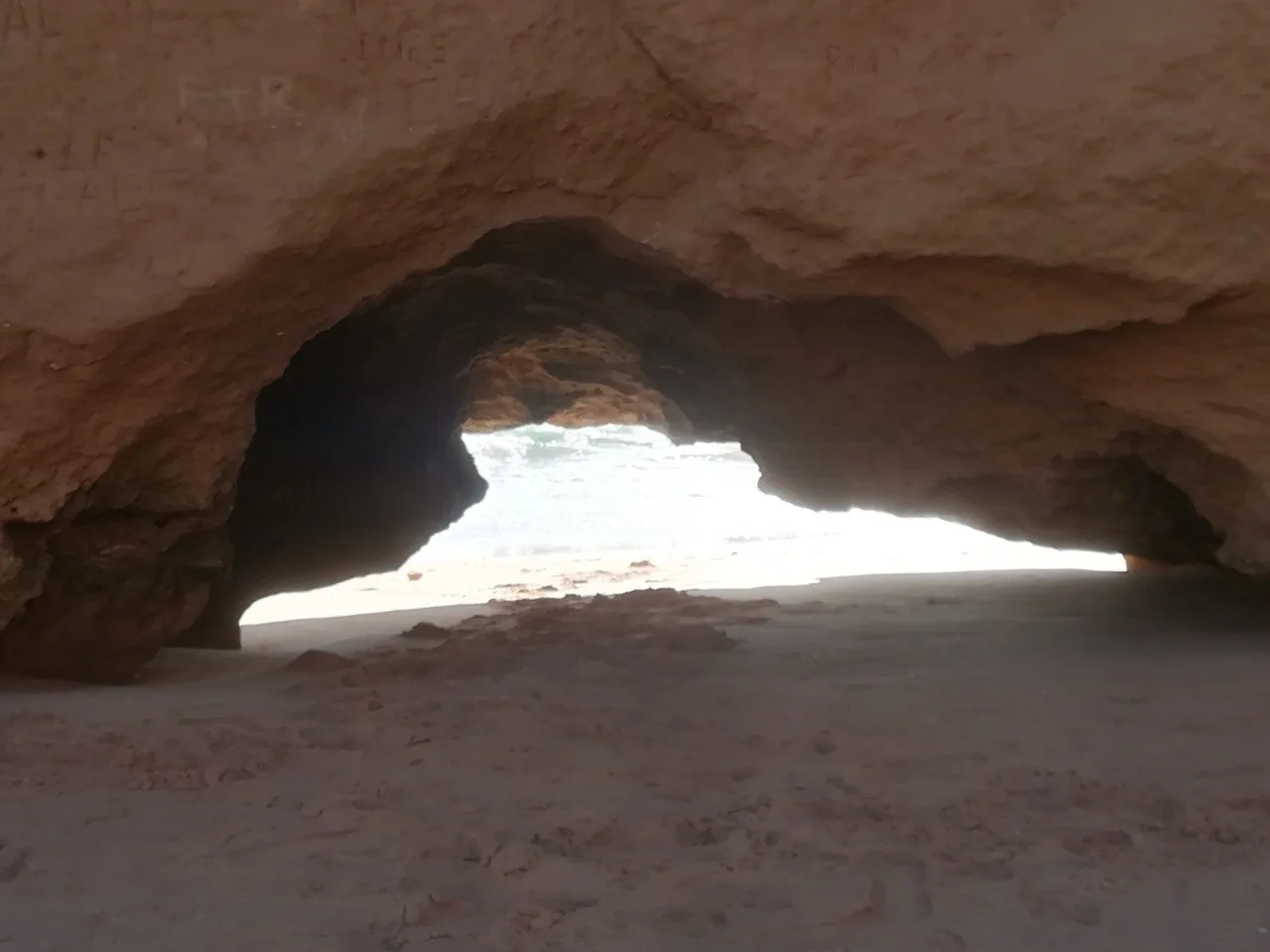 Een uitgesleten rotsboog in de zandsteen aan het strand van Portimão, met daarachter het licht van het strand