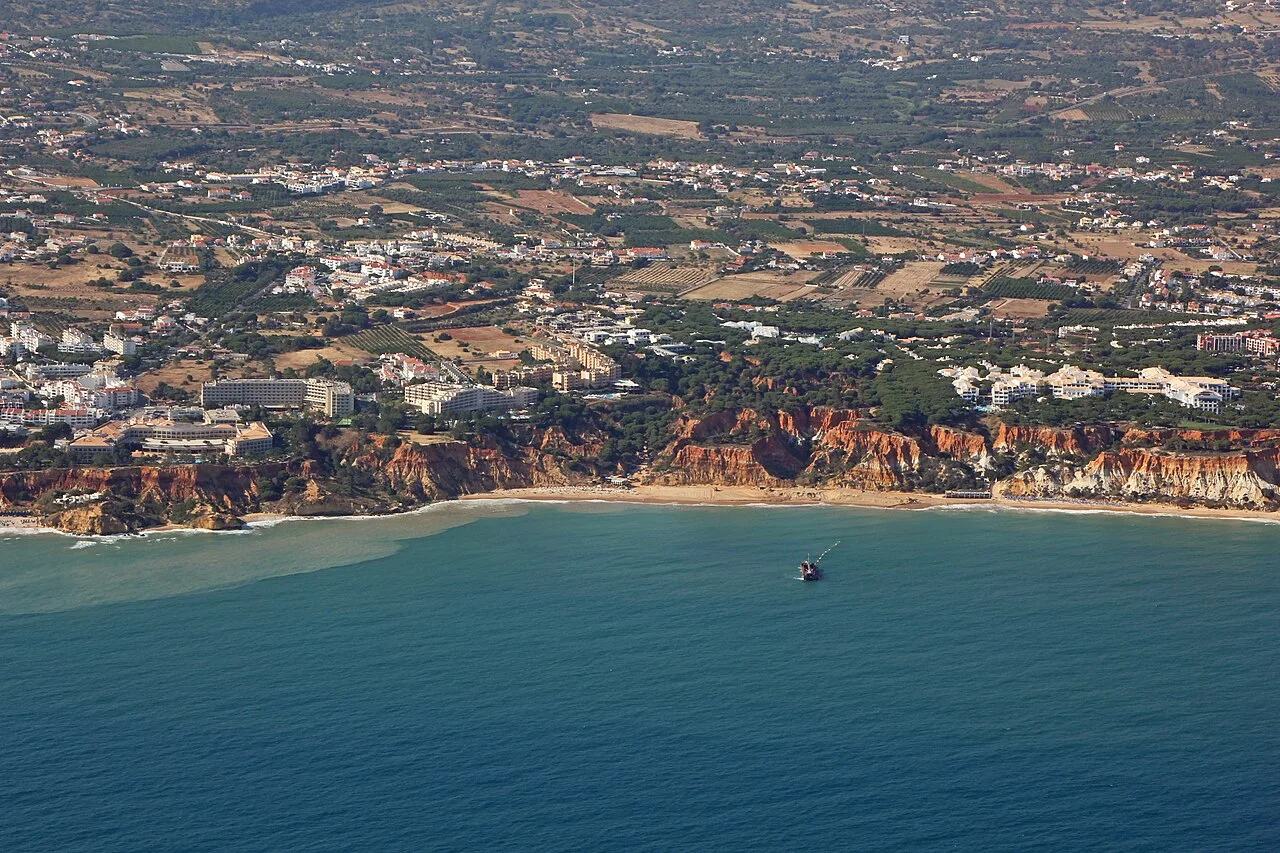 Luchtfoto van de kust bij Olhos d'Água: rode kliffen langs het strand, met hotels en woonwijken erboven