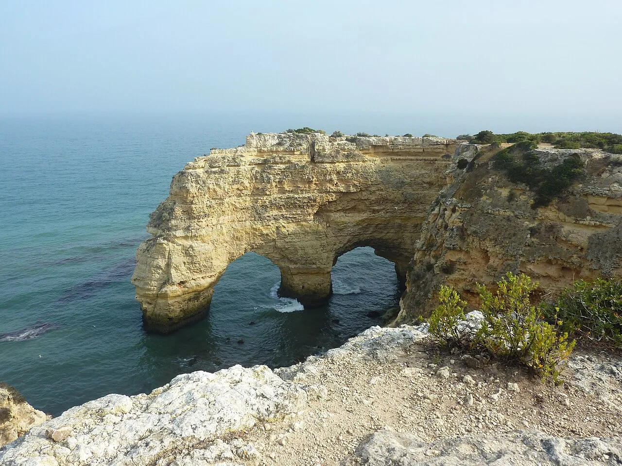 Een dubbele natuurlijke rotsboog in zee bij Praia da Marinha, gezien vanaf de klifrand