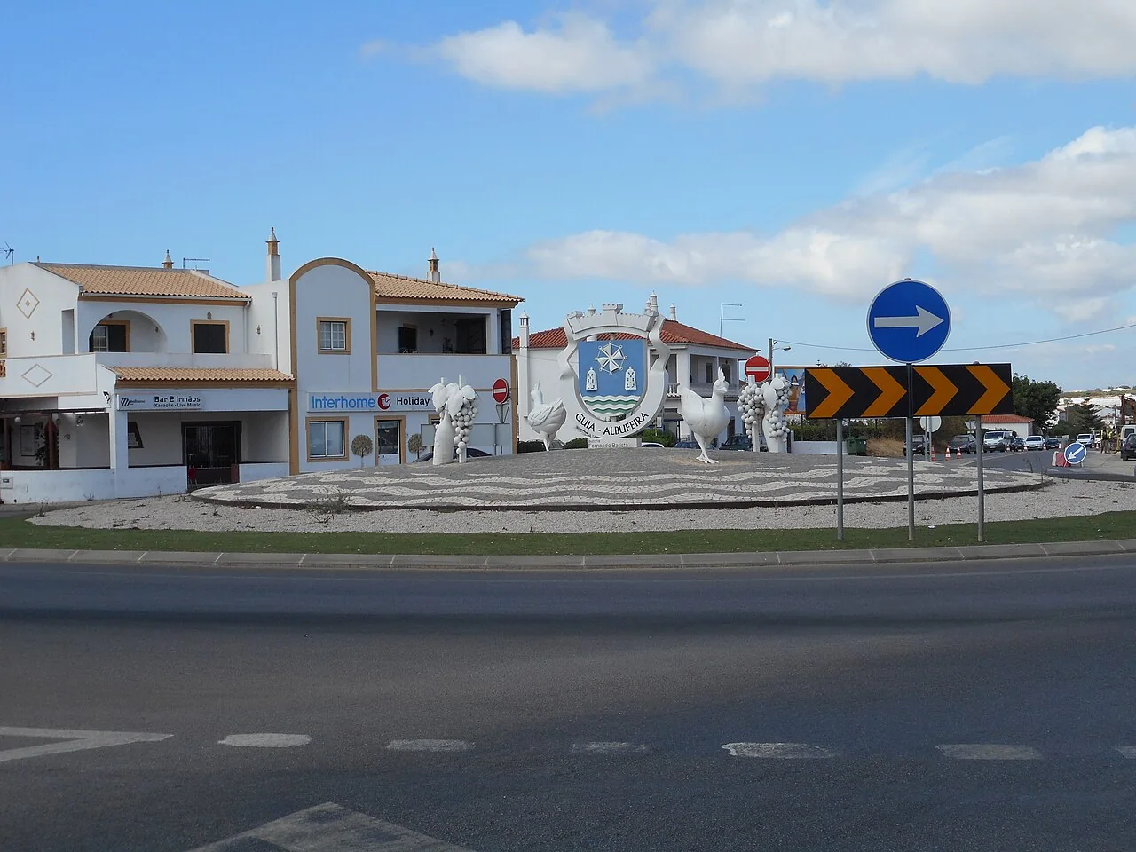 Een rotonde in het dorp Guia bij Albufeira, met een sculptuur in het midden en witte huizen eromheen