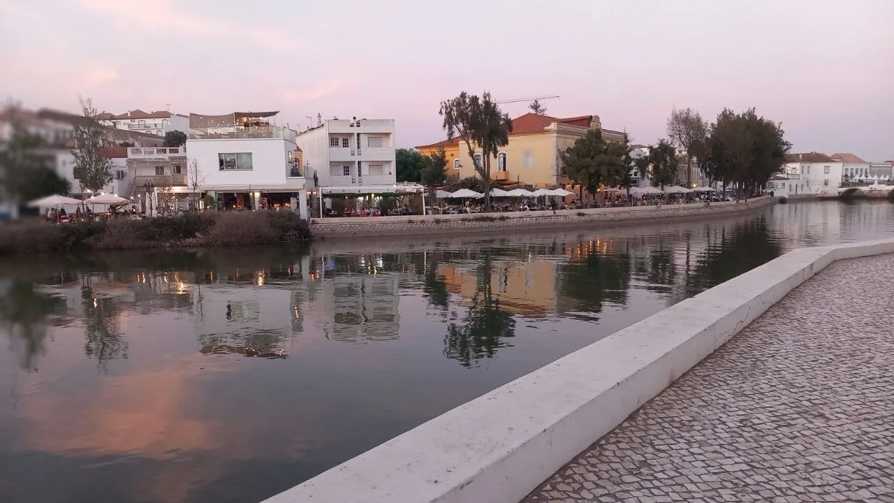 De Gilão in Tavira bij schemer, met witte huizen en terrassen langs het water en een roze lucht die weerspiegelt