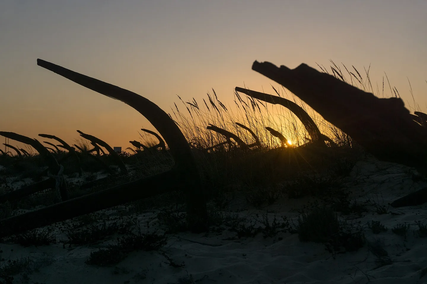 Roestende ankers van het Cemitério das Âncoras in silhouet tegen de ondergaande zon bij Praia do Barril