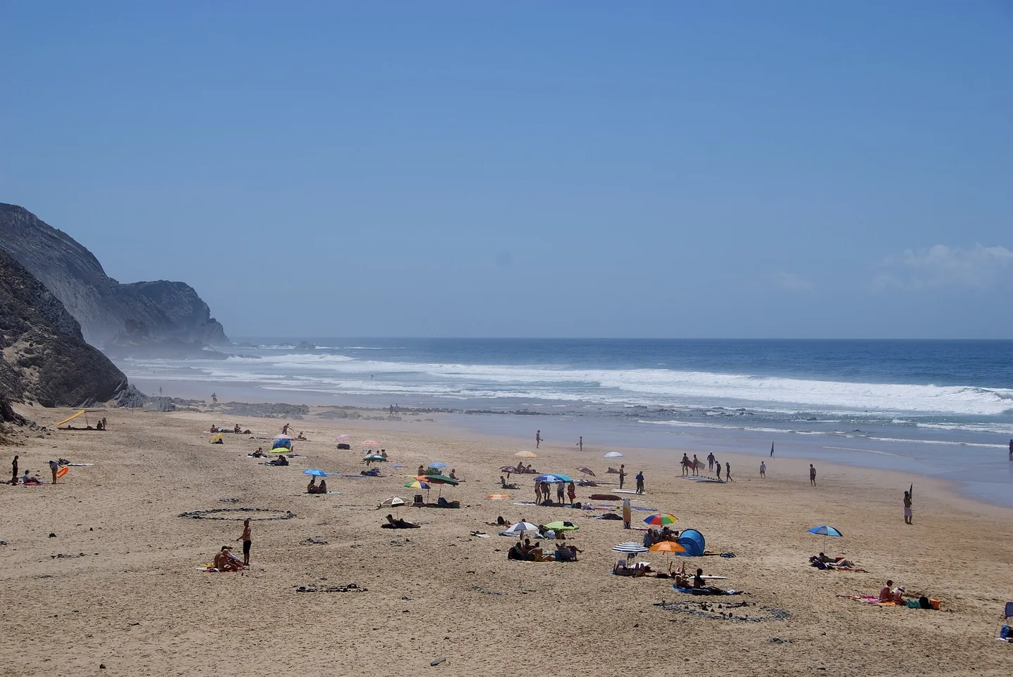 Het brede strand van Cordoama met verspreide parasols onder hoge donkere kliffen